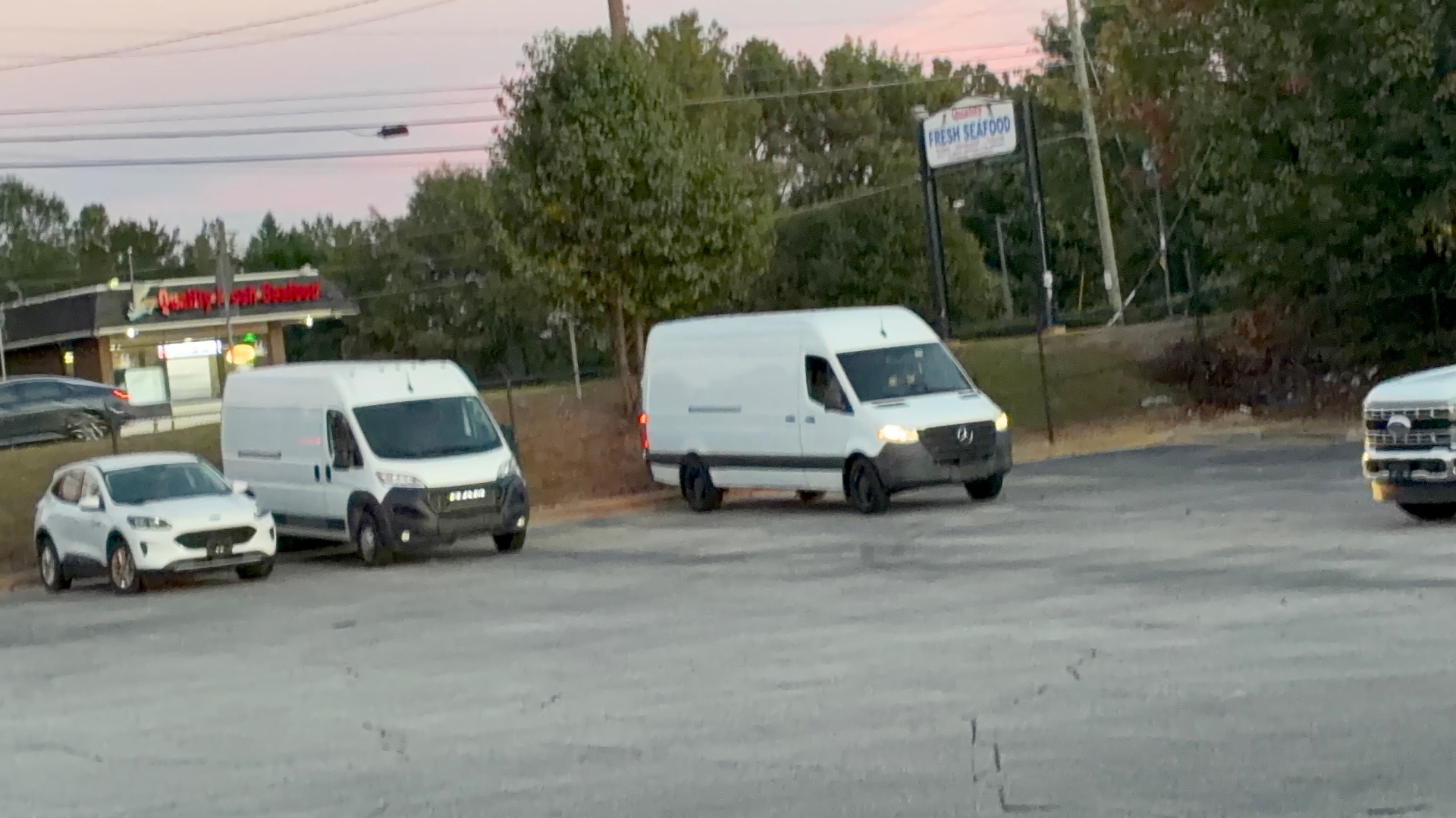 White Sprinter van driven through a Metro Atlanta lot at dusk before a flatbed tow