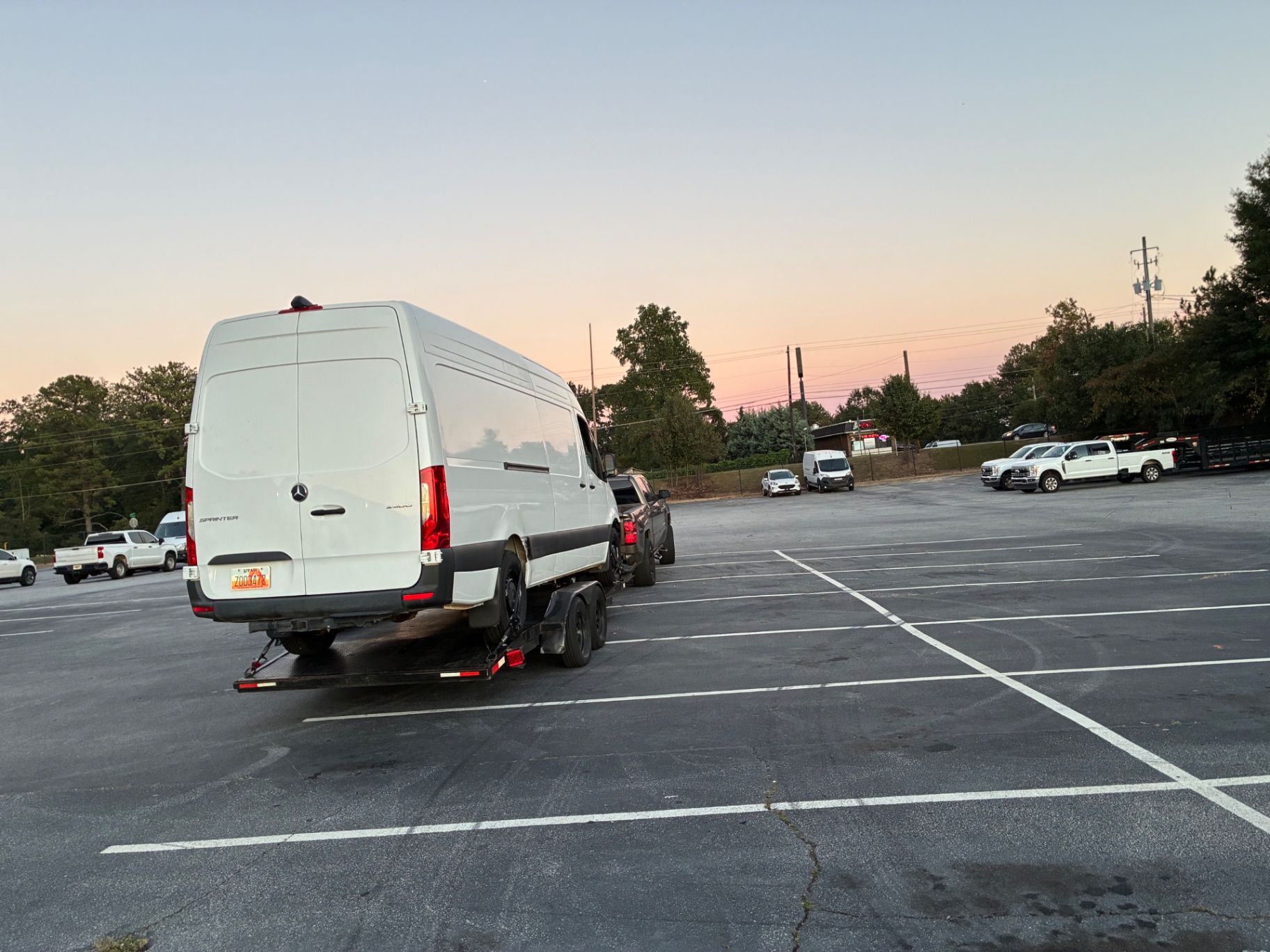 Complete tow rig with a Sprinter van on a flatbed trailer hitched to a pickup truck in a parking lot