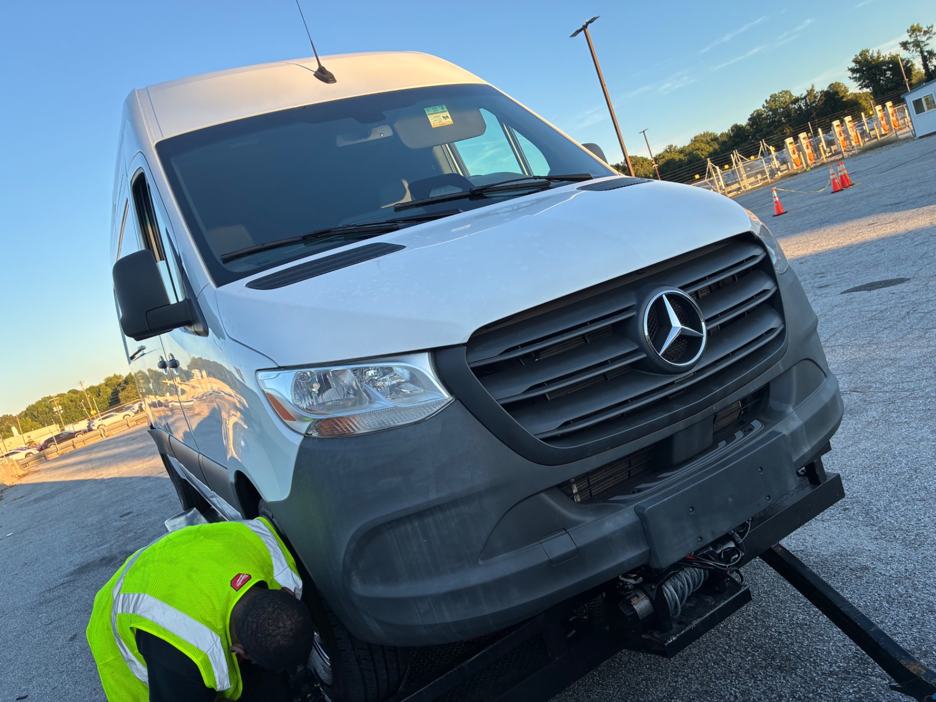 Technician in a safety vest strapping the front wheel of a Sprinter van on a flatbed tow trailer
