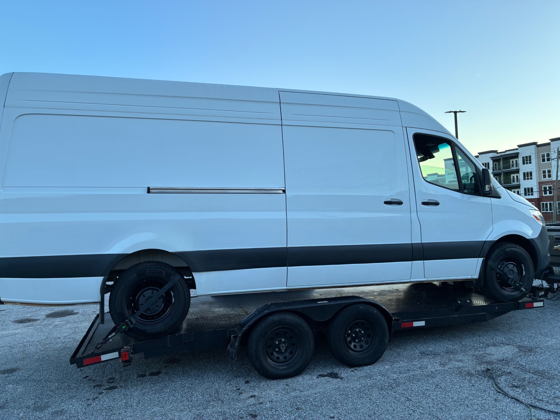 White Sprinter van secured with wheel straps on a flatbed trailer for towing