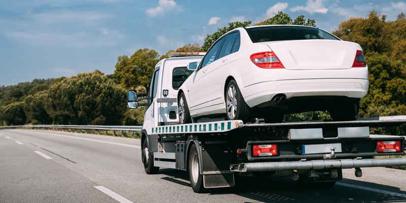 Flatbed tow truck towing a white sedan on the highway